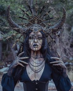 a woman with horns on her head and makeup is standing in front of some trees