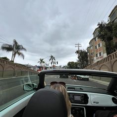 two people in a convertible car driving down the road with palm trees on either side