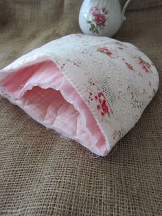 a white tea pot sitting on top of a table next to a pink flowered pillow