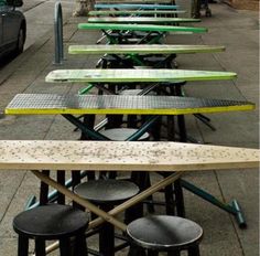 many different colored surfboards are lined up on the side of the street in front of some parked cars