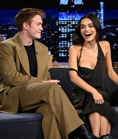 a woman sitting next to a man on a couch in front of a cityscape