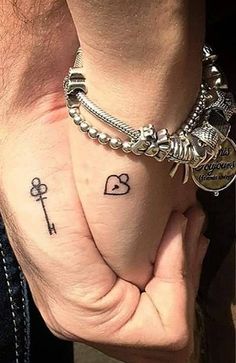 two people holding hands with tattoos on their wrists and wristbands, one has an anchor and the other has a key