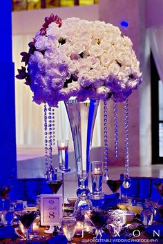 a tall vase filled with white flowers on top of a table covered in wine glasses