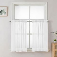 a window with white sheer curtains hanging on the side of it next to a dresser