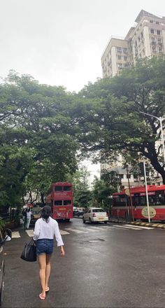 a woman walking down the street in front of two red double decker buses