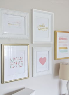 four framed pictures hang on the wall above a white desk with a lamp and two lampshade