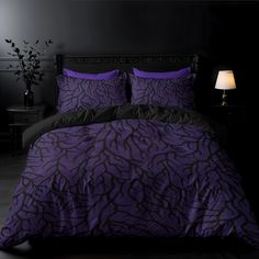 a bed with purple and black comforters in a dark room next to a lamp