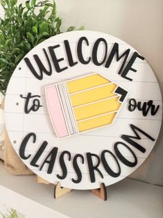 welcome to our classroom sign on a shelf with potted plant in the corner behind it