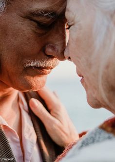 an older man and woman are touching each other's forehead as they stand close together