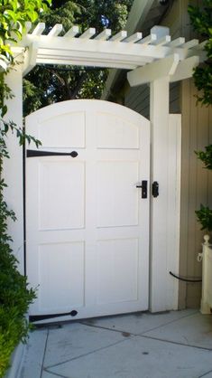 an open white door in the middle of a garden with potted plants on either side