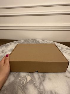 a person's hand holding a box on top of a marble table with white walls