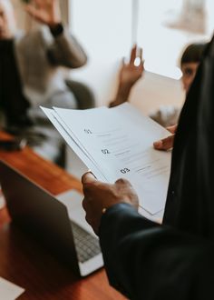 a man holding a piece of paper in his hand while sitting at a desk with other people