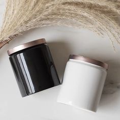 two black and white jars sitting on top of a table next to some dried grass