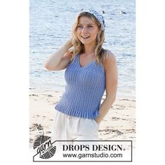 a beautiful woman standing on top of a sandy beach next to the ocean wearing a blue tank top