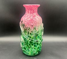 a pink and green glass vase sitting on top of a table next to a gray wall