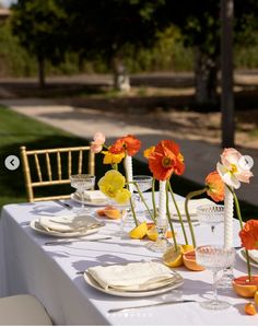 the table is set with white linens and orange, yellow, and pink flowers