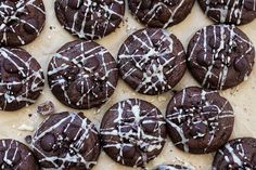 chocolate cookies with white icing and sprinkles on a sheet of parchment paper