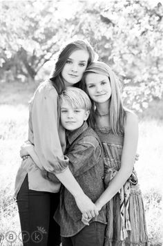 black and white photograph of three girls hugging each other in front of a field with trees