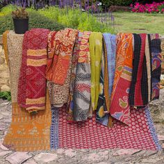 many different colored towels are hanging on a clothes line in front of some bushes and flowers