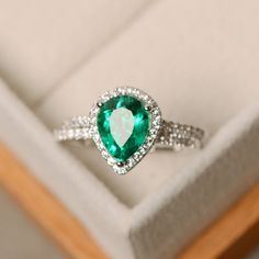 an engagement ring with a green stone surrounded by white diamonds in a gift box on top of a wooden table