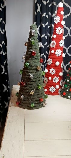 three knitted christmas trees sitting on top of a wooden table next to a window