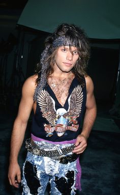 a man with long hair and tattoos on his chest standing in front of a building