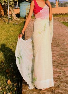 a woman in a white and pink sari walking down a brick path with her hand on her hip