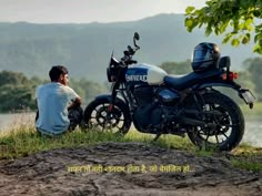 a man sitting next to a motorcycle on top of a lush green field near a lake