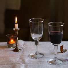 two wine glasses sitting on top of a table next to a candle and some candlesticks