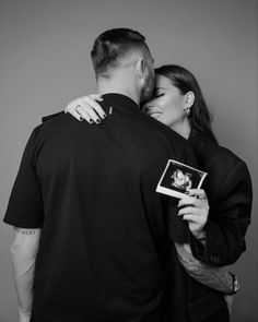 a man and woman embracing each other while holding an object in their hands, with the photo taken from behind them