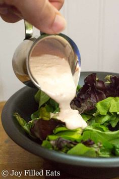 someone pouring dressing onto a salad in a bowl