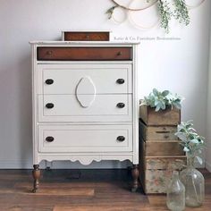 a white dresser sitting on top of a wooden floor next to two vases and a plant