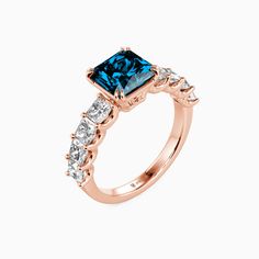 an engagement ring with blue and white diamonds on the sides, set in 18k rose gold