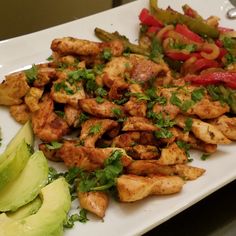 a white plate topped with chicken and veggies next to sliced avocado