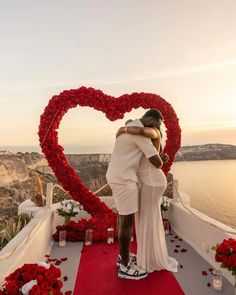 a man and woman embracing each other in front of a heart - shaped display of flowers