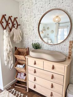 a dresser and mirror in a room with wallpapered walls, drawers and clothes hanging on hooks