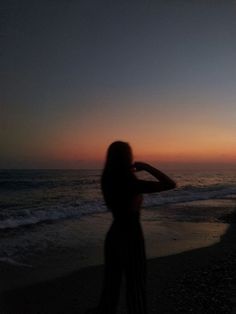 a woman standing on top of a sandy beach next to the ocean at sunset or dawn