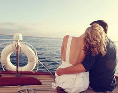 a man and woman sitting on the back of a boat looking out at the ocean