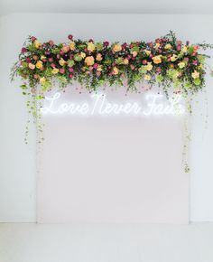 a neon sign that says lone never stay with flowers on it and greenery growing over the top