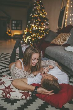 a man and woman laying on the floor next to a christmas tree