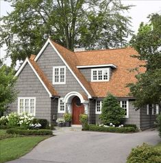 a gray house with white trim and red door is surrounded by greenery, shrubs and trees