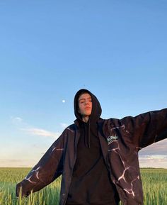 a young man standing in a field with his arms spread out to the side wearing a black hoodie