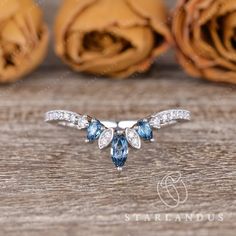 an engagement ring with blue and white stones on it, surrounded by rose petals in the background