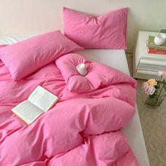 a bed with pink sheets and pillows on top of it, next to a vase filled with flowers