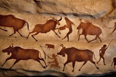 some animals and people are painted on the side of a rock wall in a cave