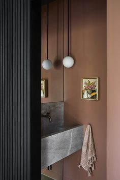 a bathroom sink sitting under two lights next to a painting on the wall above it