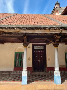 an old building with columns and green shutters on the front door is seen against a blue sky