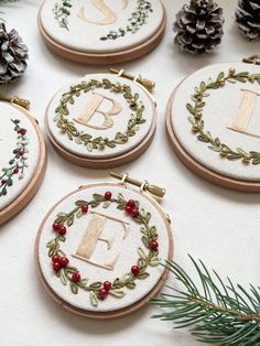 embroidered monogrammed christmas ornaments with pine cones and evergreen needles on a white surface