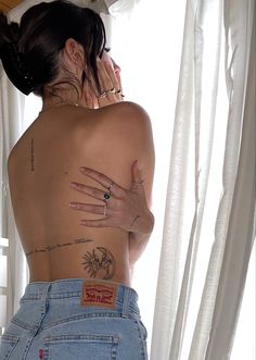 a woman with tattoos on her back standing in front of a window