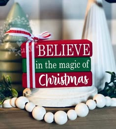 a red and green sign that says believe in the magic of christmas next to white balls